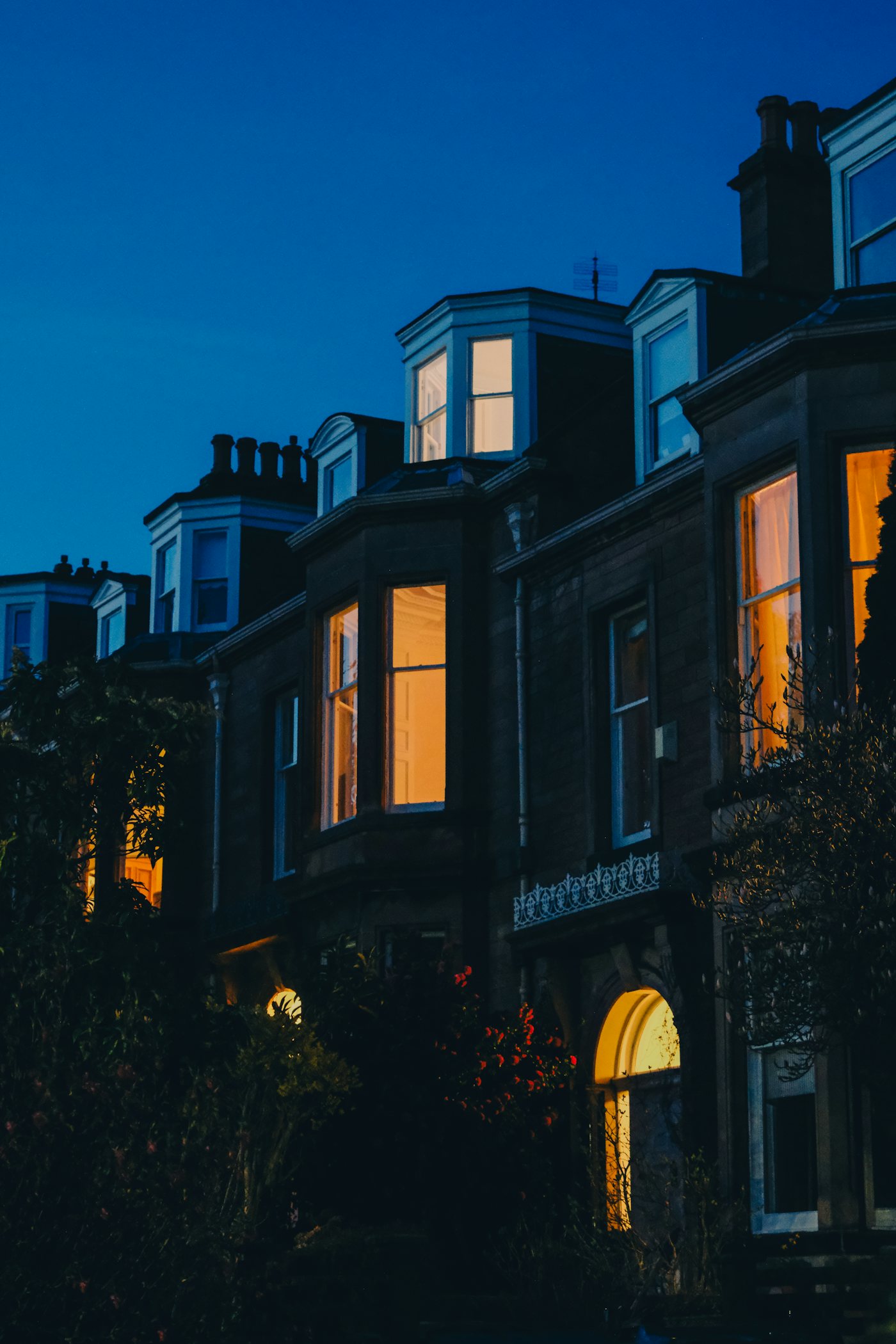 Row of townhouses at dusk, windows glowing warm against a deep blue sky